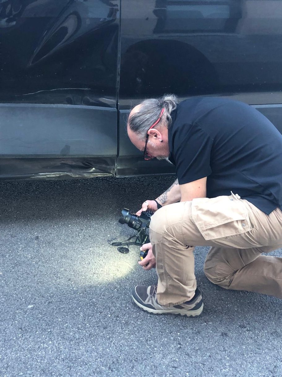 Schadenbegutachtung auf Mallorca Ein Mann kniet neben einem Auto und fotografiert einen Kratzer am Kotflügel.